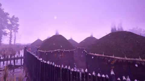 Guy Schofield Several wooden huts are in water and enclosed by a metal fence. Each hut has a fire inside. The sky is a purple colour and there are several trees.