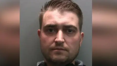 Mugshot of Andrew Miller who has brown spikey hair and a beard. 