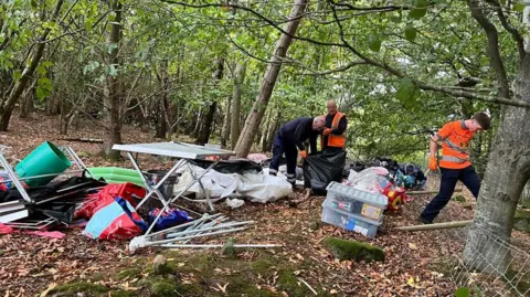 Workers in hi-vis clearing away the camp in woodland. 