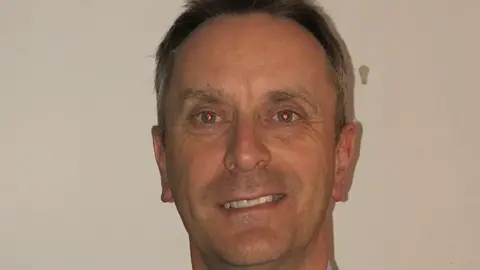 FastHouse Colin Clements has salt-and-pepper hair and is smiling at the camera. He has red-eyes due to the camera.