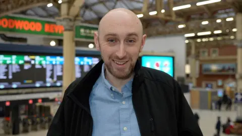 Matthew Streeton smiles whilst standing above the concourse at Victoria train station