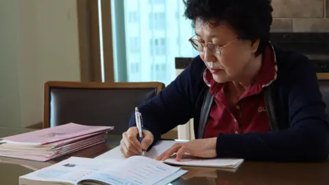 BBC Korean Han Tae-soon sits at a table practising her English by writing in a notebook, copying from an English textbook opened in front of her.