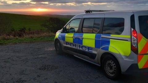 A police van sat facing a field with a sunset 