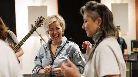 Alastair More Cora Bissett has grey, long-ish hair and is wearing a vintage denim jacket. She is laughing 