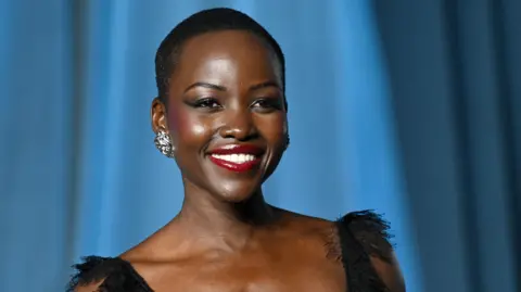 Lupita Nyong'o smiling and wearing a black dress, posing for photos at the Academy Museum of Motion Pictures in Los Angeles in October 2025