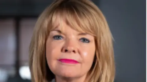 Chief executive Monica Fogarty pictured wearing bright pink lipstick. She has blonde short hair and a full fringe.