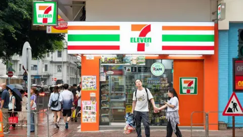 Getty Images Pedestrians walk past the Japanese-owned American international chain of convenience, 7-Eleven, store and logo in Hong Kong.