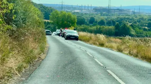 A country lane with a number of cars parked on a verge