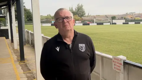 James Vincent / BBC Dave Hampshire du Penistone Church FC est au stade du club. Il porte une toison de club et a des lunettes.