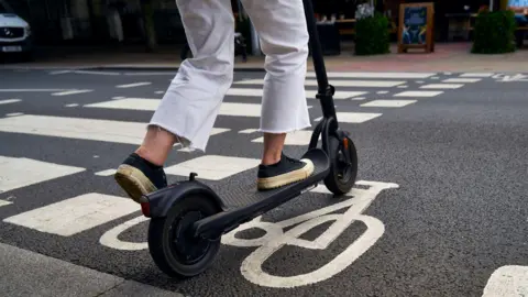 A person rides a black e-scooter in a cycle lane. 