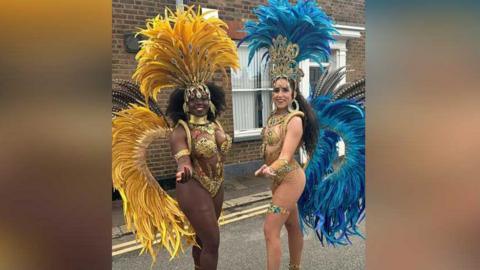 Two women dressed in carnival outfits with bright yellow and blue feathers coming off their backs and gold jewellery