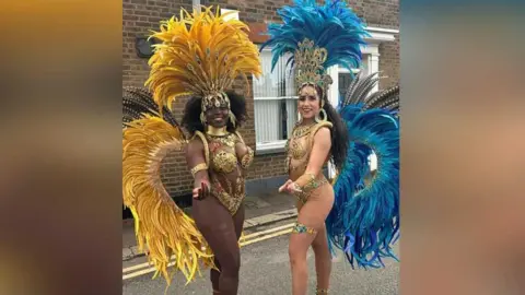 Julita Waleskiewicz/BBC Two women dressed in carnival outfits with bright yellow and blue feathers coming off their backs and gold jewellery