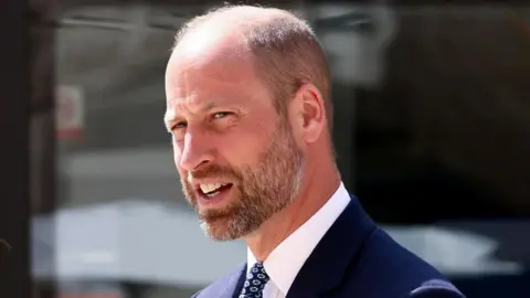 Prince William, with short light hair and beard, wears a suit.