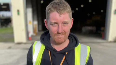 Waste warden Chris Smith wearing a black hoody and high visibility vest with short ginger hair and beard.