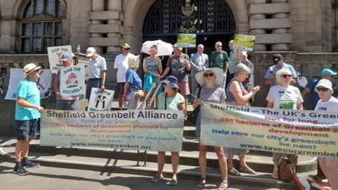 A large group of people stand on steps outside Sheffield City Hall holding banners and placards