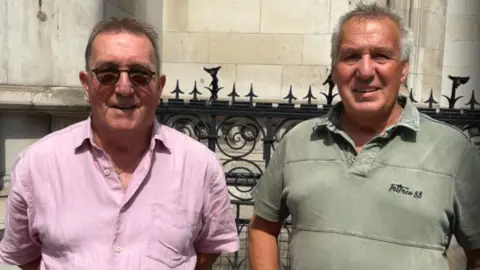Brian Farmer/BBC Billy Pither and Dave Humphreys: Two men standing in front of a black metal fence. The man on the left has short dark hair and is wearing tinted glasses and a pink, open-necked shirt. The man in the right has short greying hair and is wearing a green polo-style shirt.
