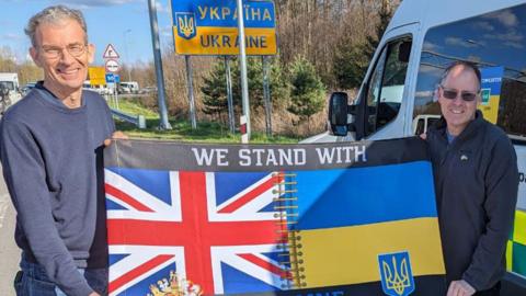 Two men holding a Union flag and Ukrainian flag in front of Ukraine border crossing