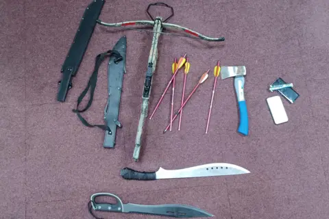 Northumbria Police Weapons, including an axe, two large knives, a crossbow and darts, on a burgundy floor.