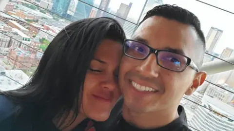 Retired Staff Sergeant Wilmer Trujillo and his wife, Arelys Barahona Martinez, in an undated photo. It is a selfie photo; Arelys smiles with her eyes closed as she leans into Sgt Trujillo, who is looking at the camera and smiling.