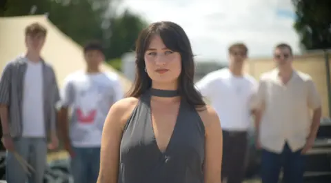 Jamie Niblock Harriet Cree, wearing a grey dress with dark hair. Her band is in the background