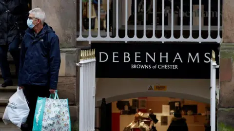 Reuters Man wearing a face protection mask and carrying two large shopping bags stands outside the entrance to Debenhams at Browns of Chester