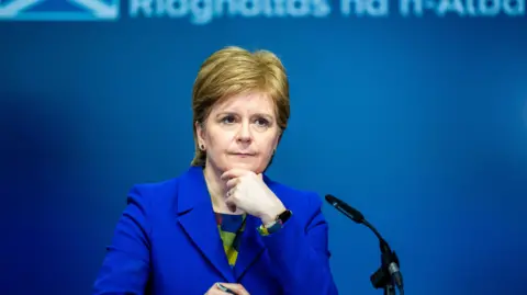 Reuters Nicola Sturgeon answering questions during a news conference at St Andrews House in Edinburgh in 2023. She is wearing a blue outfit and is standing in front of a blue background.