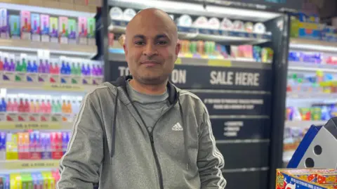 Shopkeeper Urfan Hussain at the till in his local grocery shop