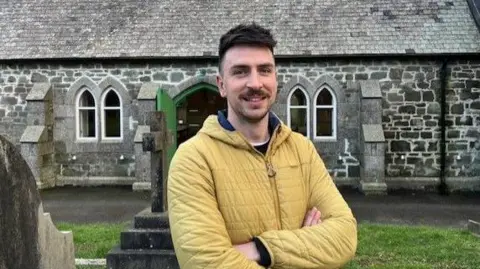 A man with a moustache stands in front of a building that used to be a chapel but is now a performance space