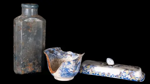 Royal Botanic Garden Edinburgh Opaque bottle on the left. A chipped bowl and the lid from a butter dish on the right. All against a black background.