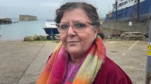 A woman standing and looking at a camera wearing glasses and a bright coloured scarf.