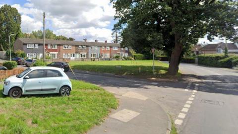 A google maps image of a t-junction in a residential area with a car parked on a green and terraced houses in the background 