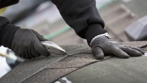 Close-up of hands cutting a roof tile with a blade