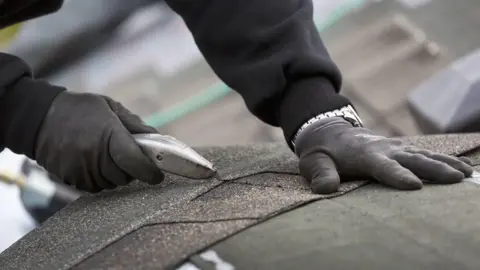 PA Media Close-up of hands cutting a roof tile with a blade