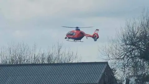 Rich Cliff A picture of an air ambulance leaving the scene. It is a red and blue helicopter.