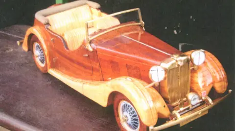 Fred Clarke A highly polished wooden and brass model of an MG Tourer saloon car with its top down.