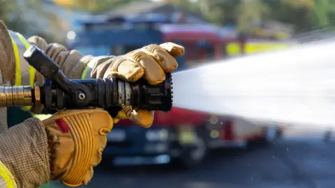 A stock image of a firefighter putting out flames with a hose.