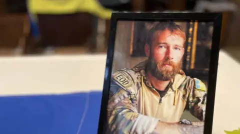 A framed phot of Chris Garrett in military fatigues placed on the alter with the blue and yellow of the Ukrainian flag in the background.