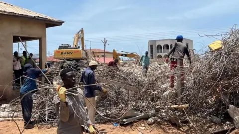 People pick steel bars as a bulldozer clears rubble at the site of the collapsed building in Accra