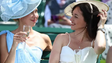 NEIL HALL/EPA/Shutterstock Two women chat with champagne glasses on the first day of Royal Ascot.