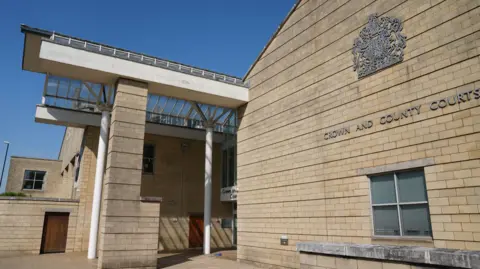 PA Media A cream brick building with the silver crest of a Crown Court on it, pictured on a sunny day.