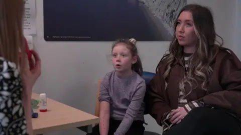 Atlanta and Amelia watch as their doctor demonstrates how to use a training whistle.