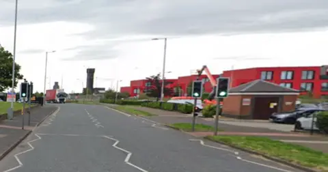 Traffic lights on green on Dock Road, with red buildings on the right and a lorry approaching in the distance.