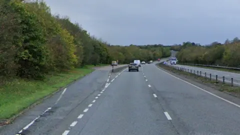 A two lane A-road, with some cars travelling along it, and a layby to the side