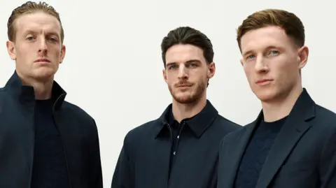 Head and upper body of three England footballers in smart dark suits coats from Marks and Spencers