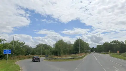 A Google street view of the A1034 slip road onto the A63 near South cave showing metal crash barriers surrounded by trees