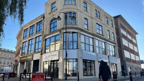 A streetscape including a grand building with three rows of windows and streets leading off on each side.