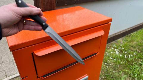 Someone putting a large knife into an orange knife amnesty bin