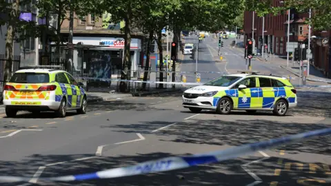 Two police cars block off a street in Nottingham city centre. Police cordon tape can be seen in the foreground and background.