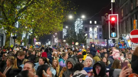 Crowds fill the streets in the city with decorations visible behind them