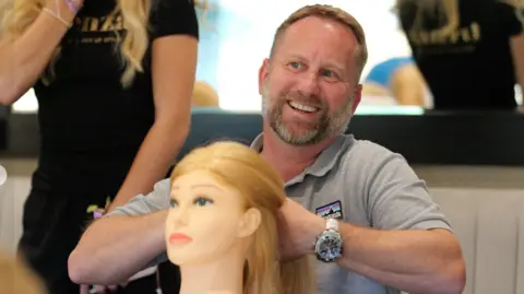 Wolves Foundation A man with a short beard wearing a grey polo shirt is smiling widely whilst facing off camera. In his hands he is holding the hair of a plastic training dummy